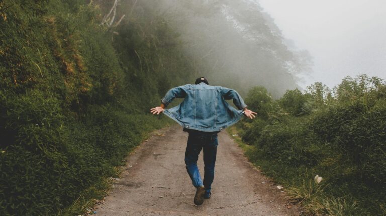 person wearing blue denim jacket while walking on foggy road